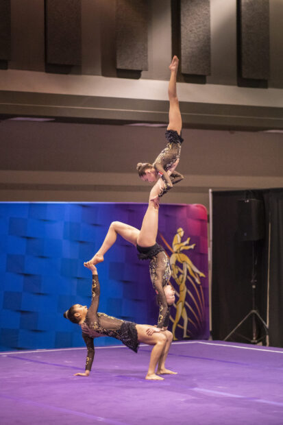 Three gymnasts perform a complex acrobatic gymnastics routine on a purple floor, 2K Mobile Wallpaper
