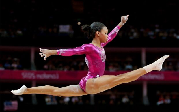 A gymnast performs a split leap in a pink outfit during an acrobatic gymnastics event, 2K Desktop Wallpaper