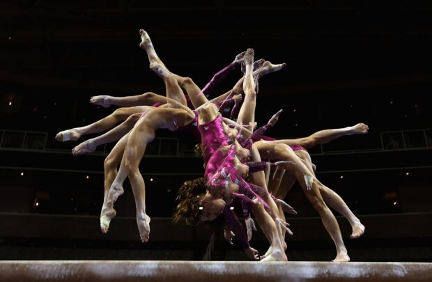 A gymnast performs a stunning acrobatic gymnastics move on the balance beam, 2K Desktop Wallpaper