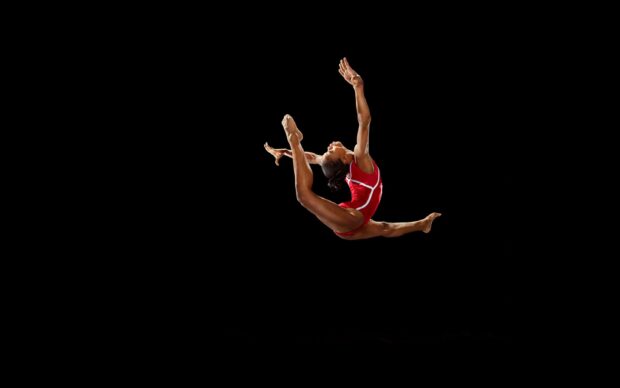 A gymnast in a red outfit performing acrobatic gymnastics in midair, 2K Desktop Wallpaper