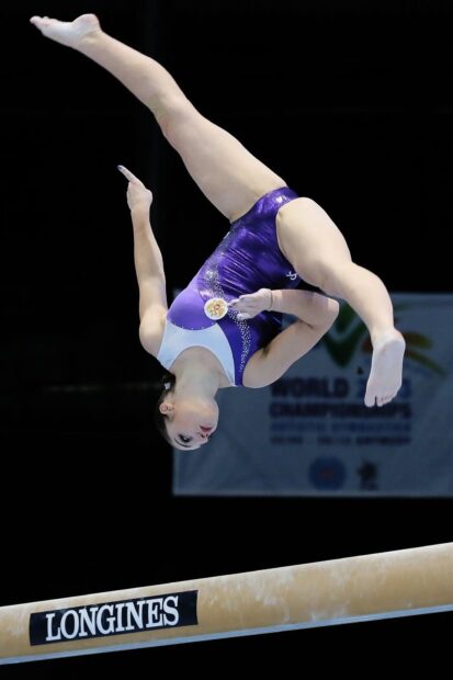 A gymnast in purple is executing an acrobatic gymnastics move on the balance beam, HD Mobile Wallpaper