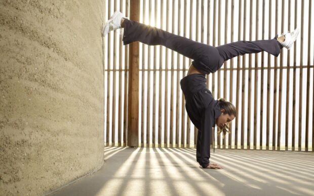 A woman practices acrobatic gymnastics in a handstand position near a wooden wall, HD Desktop Wallpaper