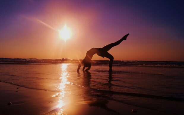 A person performs an acrobatic gymnastics pose on the beach at sunset, 2K Desktop Wallpaper
