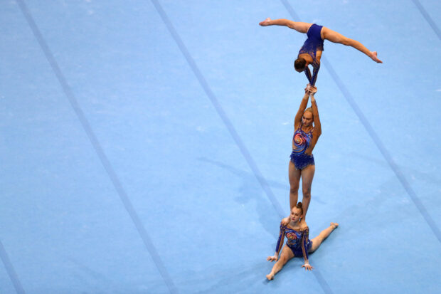 A trio of acrobatic gymnasts executing a complex balance routine on a blue mat, HD Desktop Wallpaper