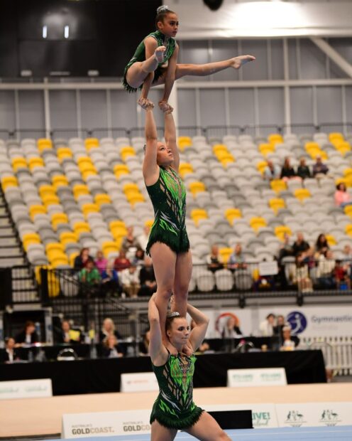 Three acrobatic gymnasts perform a balancing routine during a competition in an indoor arena, HD Mobile Wallpaper