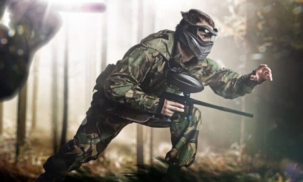 A paintball player is crouching and moving cautiously in a forest setting wearing camouflage clothing, HD Desktop Wallpaper