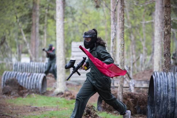 A woman playing paintball holds a red flag while running on the forest field, HD Desktop Wallpaper