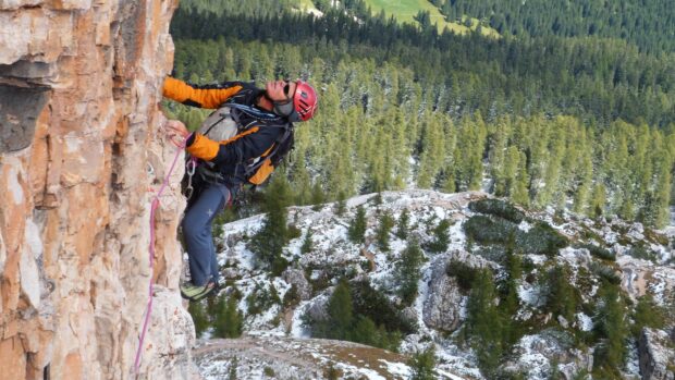 A climber wearing gear scales a rocky cliff surrounded by snowy forest in this rock climbing wallpapers, 4K Desktop Wallpaper