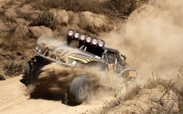 An off road driving vehicle kicks up dust in rugged desert terrain during a race, 2K Desktop Wallpaper