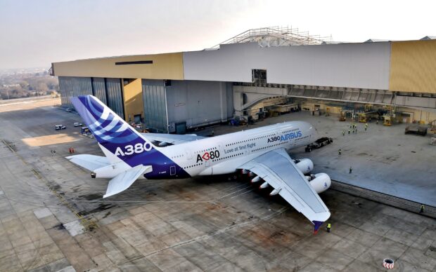 An Airbus A380 is parked near a large hangar with crew members around the aircraft, 2K Desktop Wallpaper
