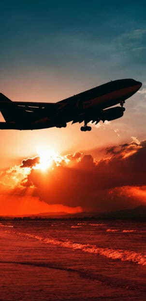 An aircraft flies over the ocean during a fiery sunset scene, 2K Mobile Wallpaper
