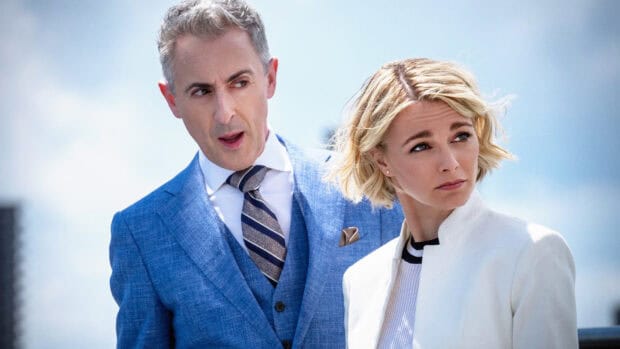 Alan Cumming stands beside a blonde woman wearing a white jacket against a blue sky, HD Desktop Wallpaper