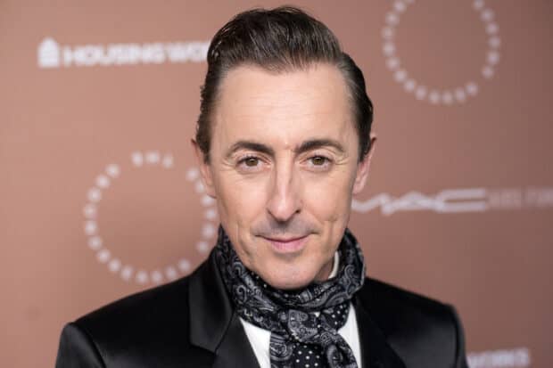 Alan Cumming wears a patterned scarf and black jacket looking at the camera, 2K Desktop Wallpaper