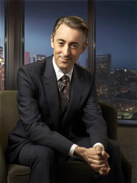 Alan Cumming sits with hands clasped in front of a cityscape at night, HD Desktop Wallpaper