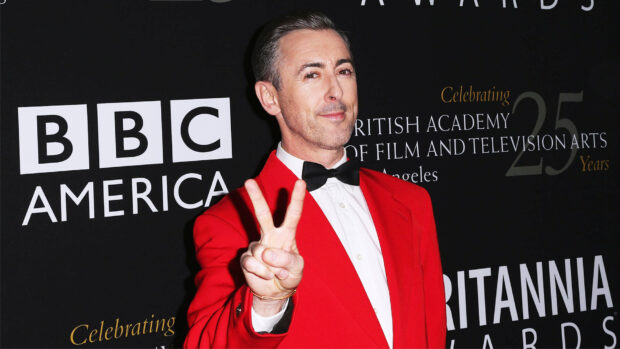 Alan Cumming is wearing a red suit and making a peace sign at an event, HD Desktop Wallpaper