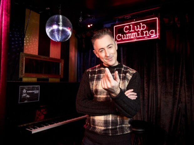 Alan Cumming smiles and gestures in a vibrant club setting, HD Desktop Wallpaper