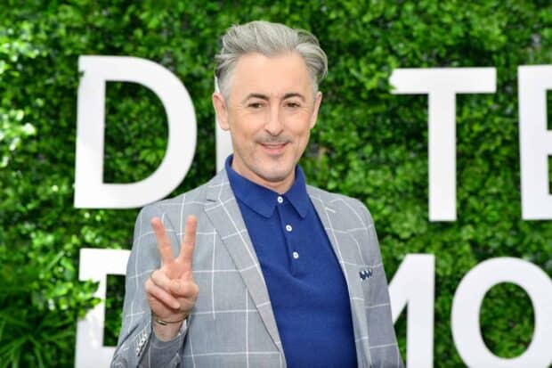 Alan Cumming poses with a peace sign in front of a green plant wall, HD Desktop Wallpaper