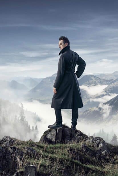 Alan Cumming standing on a rocky hill with foggy mountains in the background, 2K Mobile Wallpaper