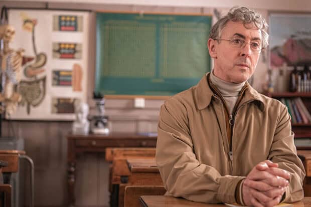 Alan Cumming is sitting in a classroom with a serious and thoughtful expression, HD Desktop Wallpaper