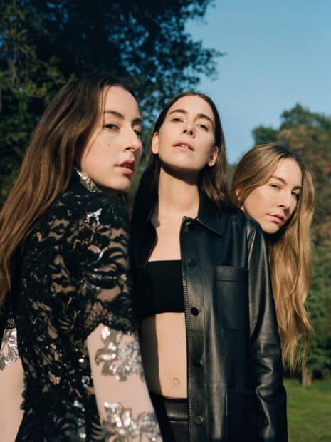 Alana Haim and her bandmates stand together posing in a natural outdoor setting, HD Desktop Wallpaper