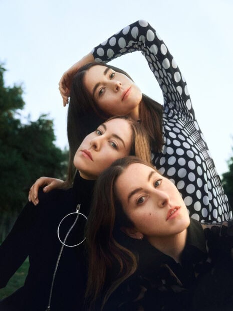 Alana Haim and her sisters are posing closely outdoors in a stylish setting, HD Mobile Wallpaper