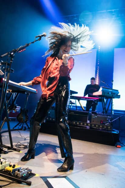 Alana Haim is energetically playing drums during a live performance on stage, 2K Mobile Wallpaper