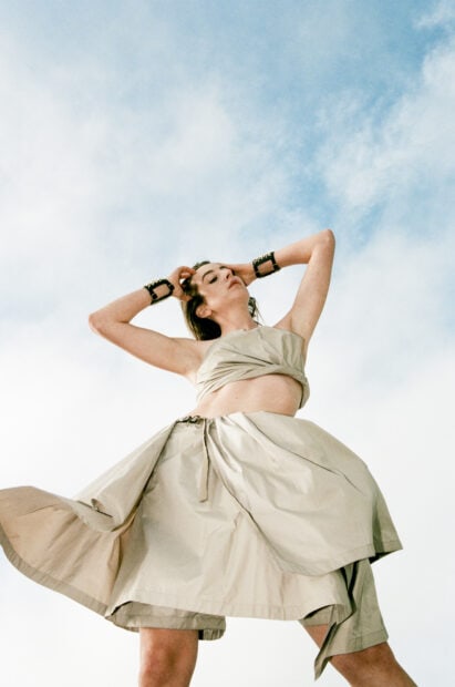 Alana Haim stands confidently with arms raised against a blue sky, HD Phone Wallpaper