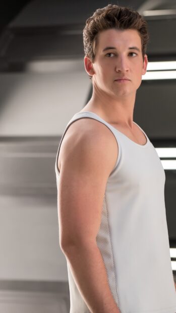 A young man wearing a white tank top stands looking sideways in a modern setting with Allegiant Wallpapers, 2K Phone Wallpaper