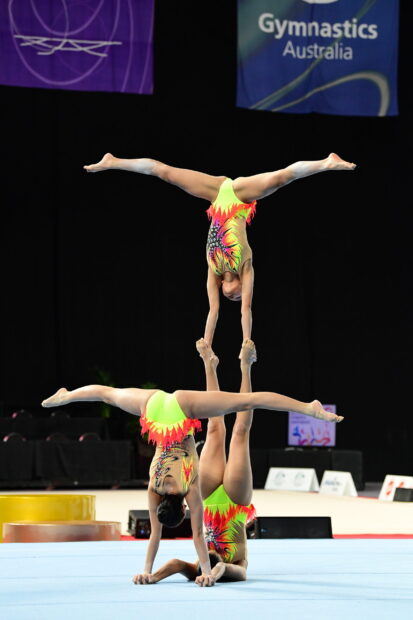 Two gymnasts perform a complex acrobatic gymnastics pose in competition, 2K Desktop Wallpaper