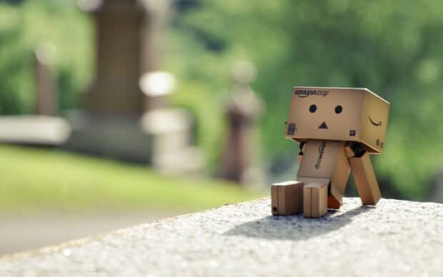 A small robot made from Amazon boxes sits outdoors on a stone surface with a blurred green background, HD Desktop Wallpaper