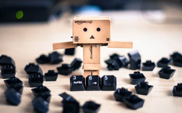 A small Danbo figure with Amazon branding stands amid scattered keyboard keys on a desk, HD Desktop Wallpaper