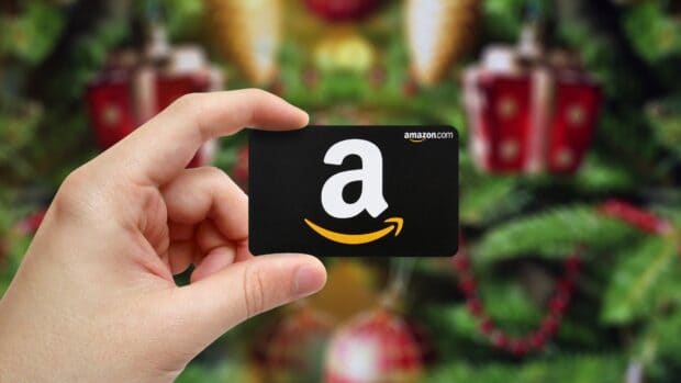 A hand is holding an Amazon card with a blurred Christmas decoration in the background showing Amazon Wallpapers, 4K Desktop Wallpaper