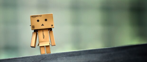 A small Amazon figure made of cardboard is standing on a surface with a blurred background, 2K Desktop Wallpaper