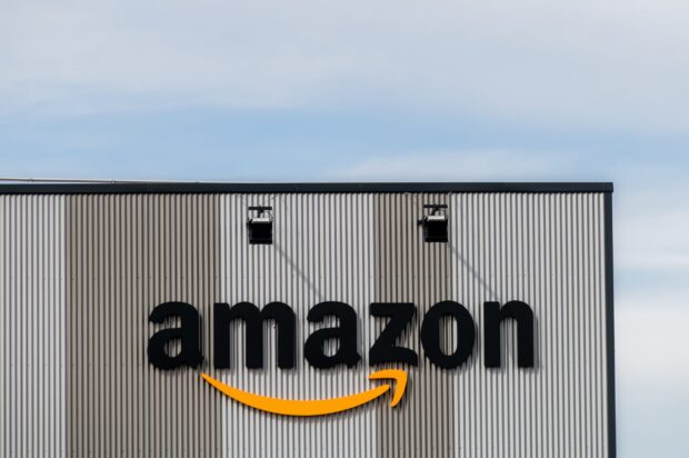 The Amazon logo is displayed prominently on a gray building wall under a clear sky, 2K Desktop Wallpaper