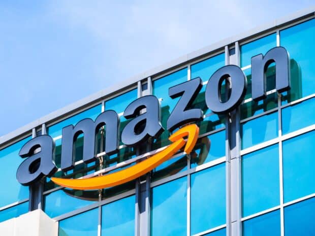The Amazon logo is displayed on a blue glass office building under a clear sky, HD Desktop Wallpaper