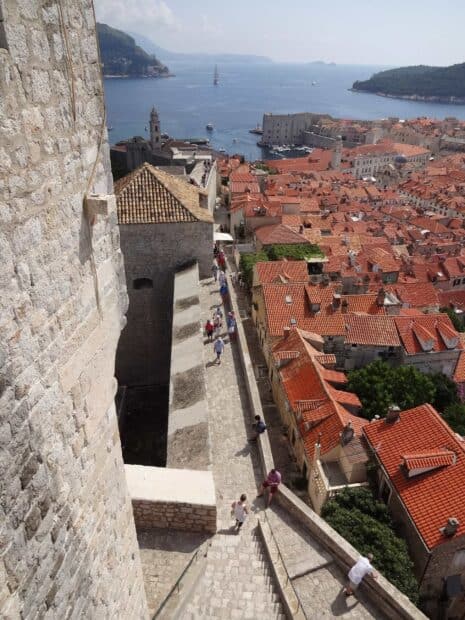 Tourists walking on ancient city walls in Dubrovnik overlooking rooftops, 2K Mobile Wallpaper