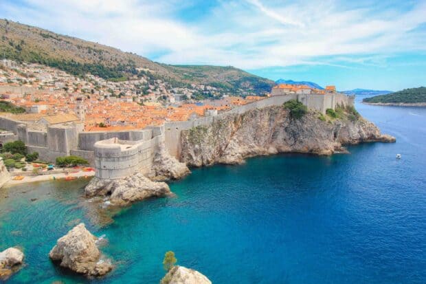 The ancient city walls in Dubrovnik rise above the clear blue sea surrounding the historic town, 2K Desktop Wallpaper