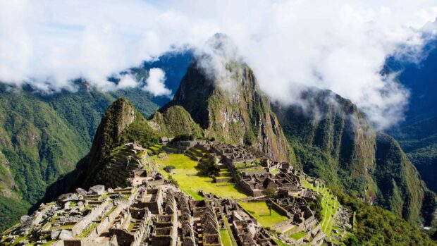 The ancient Machu Picchu ruins are surrounded by lush green mountains under a cloudy sky in Peru, 4K Desktop Wallpaper