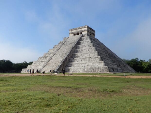 The ancient Mayan pyramid at Chichen Itza stands tall against a clear sky with people walking nearby, HD Desktop Wallpaper