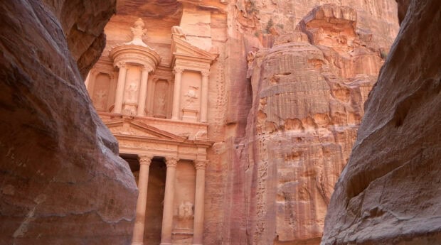 The ancient carved architecture of Petra in Jordan is shown between rocky cliffs, HD Desktop Wallpaper