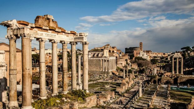 The Rome skyline displays ancient ruins under a clear blue sky, featuring historic columns and architecture, 2K Desktop Wallpaper