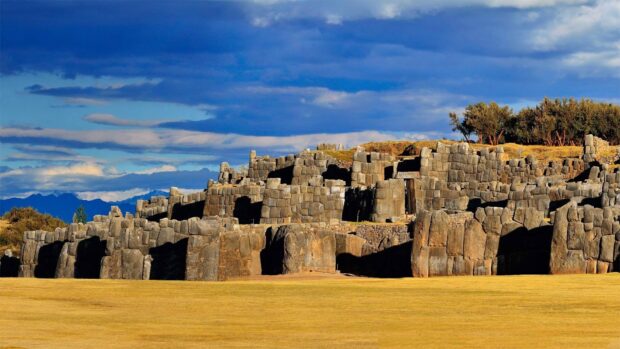 The image shows ancient stone ruins in Peru under a blue sky with clouds, HD Desktop Wallpaper