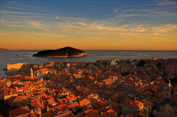 The ancient city walls in Dubrovnik glow warmly under a sunset sky with the sea in the background, 2K Desktop Wallpaper