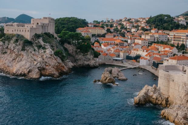 The ancient city walls in Dubrovnik surround rocky cliffs and clear blue water, HD Desktop Wallpaper