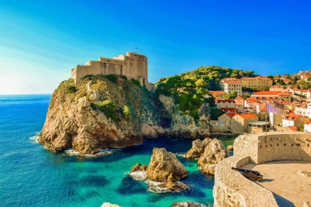 The ancient city walls of Dubrovnik overlook the crystal clear sea and rocky coastline, HD Desktop Wallpaper