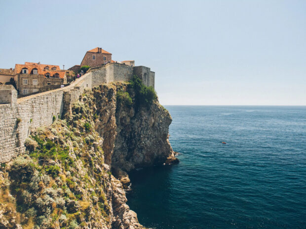 The ancient city walls of Dubrovnik stand tall on the rocky coast overlooking the deep blue sea, HD Desktop Wallpaper