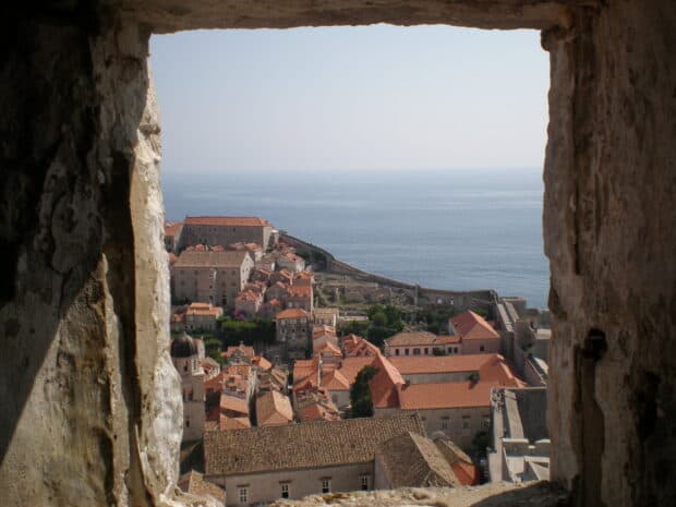 The ancient city walls of Dubrovnik overlook the terracotta rooftops and the blue sea beyond, HD Desktop Wallpaper