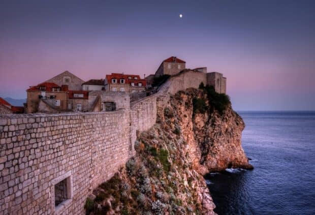 The ancient city walls in Dubrovnik rise above the rocky coastline under a colorful sky, HD Desktop Wallpaper