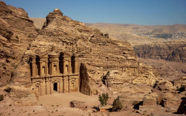 The ancient rock cut architecture in Petra Jordan stands out against a clear blue sky in a desert landscape, 2K Desktop Wallpaper