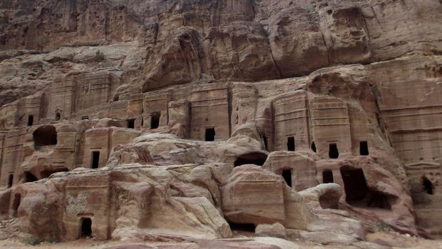 The image shows ancient rock tombs carved into sandstone cliffs in Petra Jordan, 2K Desktop Wallpaper